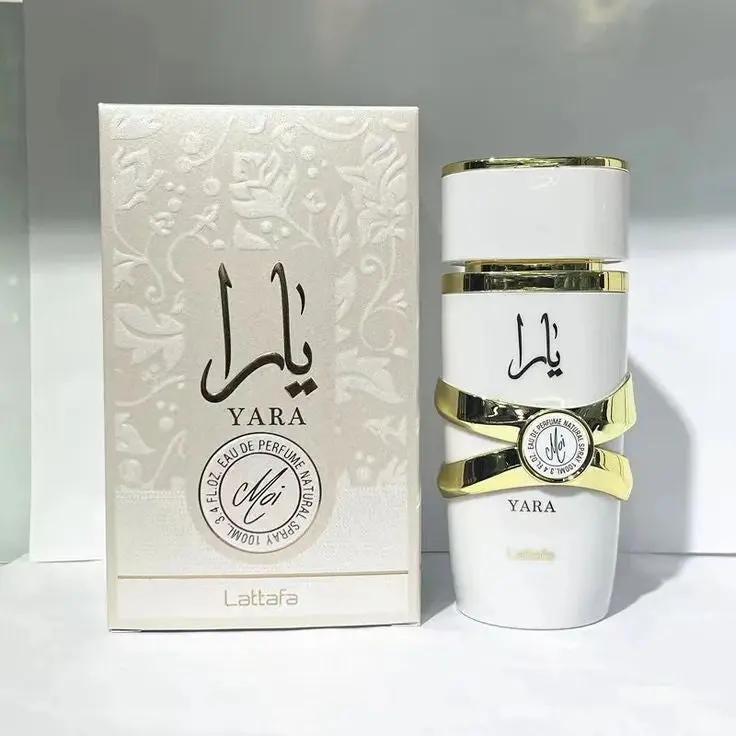 A white and gold bottle of Royal Oud Perfumes Lattafa YARA MOI gourmand floral perfume stands beside its matching decorative box, both adorned with Arabic script and elegant gold accents.