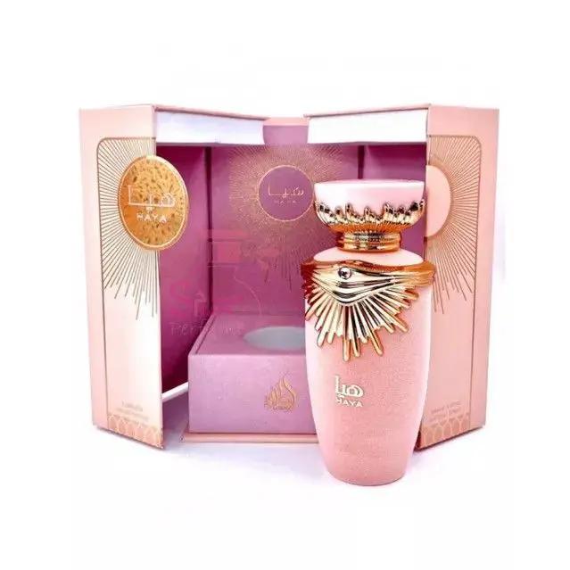 A luxurious pink Lattafa HAYA perfume bottle with gold accents and ornate cap by Royal Oud Perfumes stands before its open, matching pink and gold box, featuring Arabic text and decorative designs.