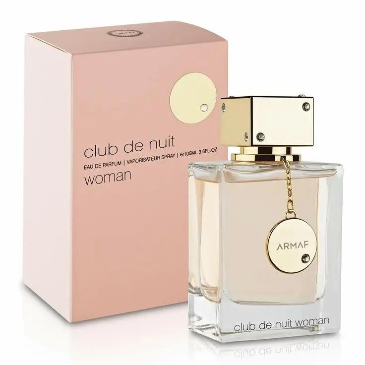 A bottle of Armaf CLUB DE NUIT WOMAN by Royal Oud Perfumes, featuring a gold cap and circular tag, sits before its pink and gold box. This elegant perfume femenino holds a light amber liquid.